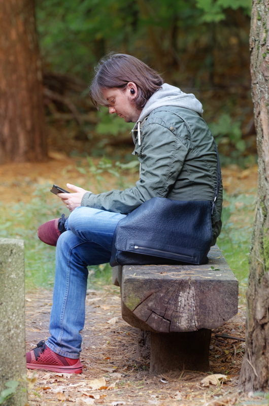15 - Person looking at a smartphone while sitting on a wooden bench in a wooded area